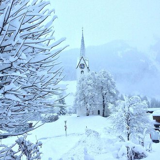 © Jockl Metzger A snowy landscape with a church in the background. Trees and bushes are completely covered in snow. | © Jockl Metzger