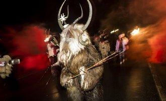 © Kleinwalsertal Tourismus | Dominik Berchtold A festive parade with masked participants in animal costumes. The dark background is illuminated by red flares. | © Kleinwalsertal Tourismus | Dominik Berchtold