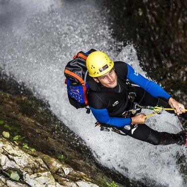Ein Mann klettert an einer steilen Felswand in einem Wasserfall. Er trägt einen Helm und eine Kletterausrüstung. | © Bergschule Kleinwalsertal | Dominik Berchtold