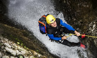 Ein Mann klettert an einer steilen Felswand in einem Wasserfall. Er trägt einen Helm und eine Kletterausrüstung. | © Bergschule Kleinwalsertal | Dominik Berchtold