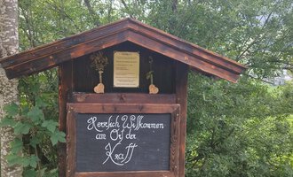 Ein traditionelles Holzschild mit der Aufschrift "Herzlich Willkommen an den Ötztal". Umgeben von grünen Bäumen und einer ländlichen Umgebung. | © Nicole Lughammer