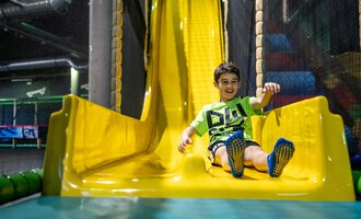 © Wonnemar Sonthofen | interSPA Gruppe A cheerful boy slides down a yellow slide in a playground. The space is designed to be colorful and inviting. | © Wonnemar Sonthofen | interSPA Gruppe