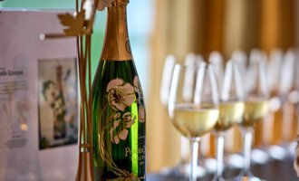 An elegant bottle of sparkling wine in a stylish display, surrounded by glasses. The background features a warm, inviting room. | © Hotel Birkenhöhe | Annette Sandner