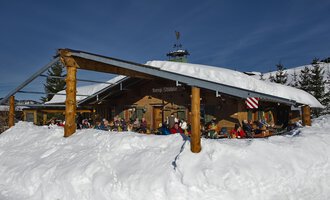 © Bergstüble | Michaela Beck Dornach A cozy mountain cabin in the snow with many people on the terrace. The surroundings are wintry and the sun is shining in the blue sky. | © Bergstüble | Michaela Beck Dornach