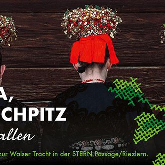 Eine Ausstellung zur Walser Tracht mit drei Personen, die traditionelle Kleidung und aufwendig gestaltete Kopfbedeckungen tragen. Der Hintergrund ist holzfarben und die Farben der Kleidung sind auffällig.