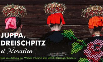 Eine Ausstellung zur Walser Tracht mit drei Personen, die traditionelle Kleidung und aufwendig gestaltete Kopfbedeckungen tragen. Der Hintergrund ist holzfarben und die Farben der Kleidung sind auffällig.