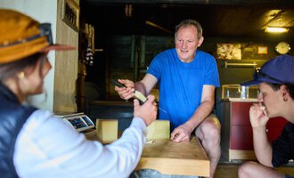 A man explains something while two people listen attentively. The scene takes place in a rustic interior. | © Kleinwalsertal Tourismus eGen - Fotograf: Oliver Farys