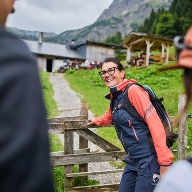 Ein gemütliches Berghaus umgeben von grünen Wiesen und hohen Bergen. Im Vordergrund führt ein Weg zur Haustür, und eine Fahne weht im Wind. | © Kleinwalsertal Tourismus eGen - Fotograf: Oliver Farys