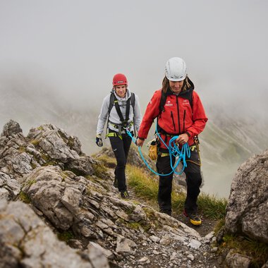 Zwei Bergsteiger bewegen sich an einem felsigen Hang. Es ist neblig und die Umgebung wirkt wild und unberührt. | © Bergschule Kleinwalsertal | Oliver Farys