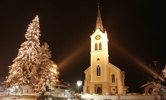 © Kleinwalsertal Tourismus | Frank Drechsel A snowy landscape with a illuminated church and a decorated Christmas tree. The night sky enhances the festive atmosphere. | © Kleinwalsertal Tourismus | Frank Drechsel