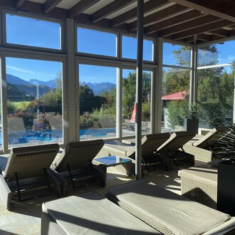 Ein gemütlicher Entspannungsbereich mit Liegen und großen Fenstern. Im Hintergrund sind Berge und ein Pool sichtbar. | © Wonnemar Sonthofen | interSPA Gruppe