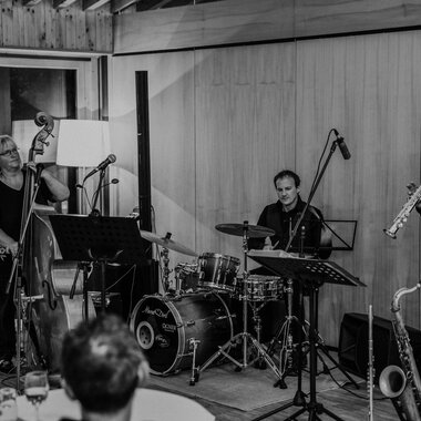 Drei Musiker stehen fröhlich zusammen und spielen verschiedene Instrumente. Im Hintergrund ist das Naturhotel zu sehen. | © Naturhotel Chesa Valisa