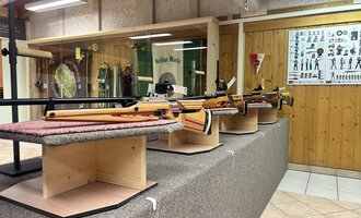 Eine Reihe von Sportgewehren auf Ausstellungsständern in einem Schießstand. Im Hintergrund sind Anleitungen und Informationen über den Schießsport zu sehen. | © Luftgewehrstand | Michael Veit