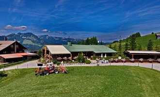 Ein gemütliches Bauernhaus mit einem großen grünen Rasen und Blick auf die Berge. Im Vordergrund steht ein Traktor und es gibt einige Sitzmöglichkeiten im Freien. | © Bergstüble | Michaela Beck