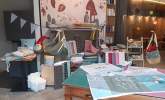 © Der Kleinwalsertaler Rosenhof | Dominik Berchtold A cozy room with various fabrics, bags, and decorations. On the wall, colorful patterns and a small doll can be seen. | © Der Kleinwalsertaler Rosenhof | Dominik Berchtold