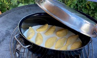Ein Topf mit gefüllten Teigtaschen wird auf einem Grill geöffnet. Im Hintergrund sind grüne Pflanzen und Blumen zu sehen. | © Gerd am Herd | Gerd Hammerer