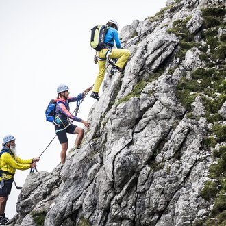 © Bergschule Kleinwalsertal | Dominik Berchtold Drei Kletterer erklimmen einen steilen Felsen. Sie tragen Helme und Kletterausrüstung, während sie sich sicher an Seilen festhalten. | © Bergschule Kleinwalsertal | Dominik Berchtold