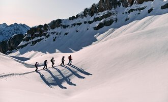Eine Gruppe von Wanderern geht über eine schneebedeckte Landschaft. Im Hintergrund sind majestätische Berge zu sehen. | © Kleinwalsertal Tourismus eGen | Oliver Farys