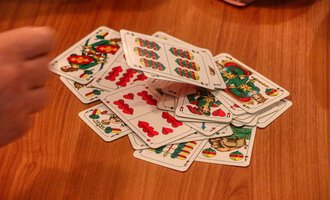 A stack of cards lies on a wooden table. A hand is visible, encircling the cards. | © Chesa Valisa