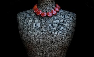 Eine kunstvolle Darstellung eines Mannequins, das mit Worten über Kunst bedeckt ist. Es trägt eine auffällige Kette aus roten Perlen. | © Gerti Maitz