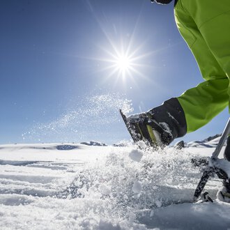 A sunny day in the snow with a person working in the snow with a ski pole. In the background, another person can be seen. | © Kleinwalsertal Tourismus | Dominik Berchtold