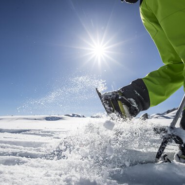 A sunny day in the snow with a person working in the snow with a ski pole. In the background, another person can be seen. | © Kleinwalsertal Tourismus | Dominik Berchtold