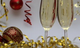 Zwei Sektgläser stoßen auf einem festlich dekorierten Tisch an. Im Hintergrund sind rote Weihnachtskugeln und goldene Dekoration zu sehen. | © Genuss- & Aktivhotel Sonnenburg