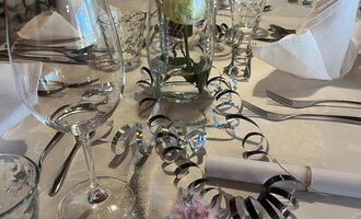 © Genuss- & Aktivhotel Sonnenburg Two champagne glasses toast on a festively decorated table. In the background, red Christmas ornaments and golden decorations can be seen. | © Genuss- & Aktivhotel Sonnenburg