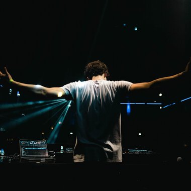 © dj let´s fetz A DJ stands behind his mixing console with outstretched arms. Colorful lights shine in the background, creating a festive atmosphere. | © dj let´s fetz
