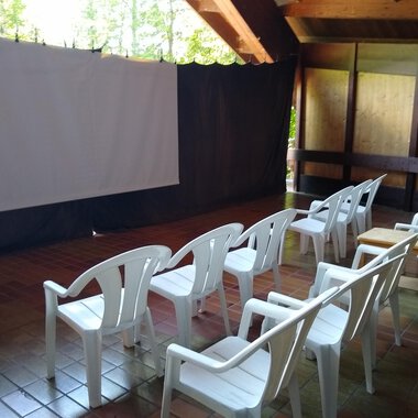 Ein Raum mit weißen Kunststoffstühlen und einer Leinwand. Die Umgebung ist ruhig und eignet sich gut für Präsentationen oder Filme. | © Kulturcafe Kleinwalsertal | Gerhard Bauer