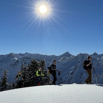 © Abenteuer Vertical | Christian Kohler A group of hikers stands on a snow-covered summit under bright sunlight. In the background, snow-covered mountains can be seen. | © Abenteuer Vertical | Christian Kohler