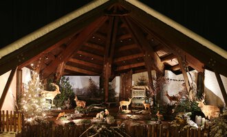 Eine festliche Kulisse mit einer Holzkonstruktion und beleuchteten Tieren. Im Hintergrund sind Weihnachtsbäume und eine winterliche Landschaft zu sehen. | © Kleinwalsertal Tourismus | Frank Drechsel