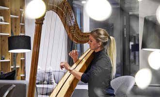 Eine Frau spielt Harfe in einem modernen Raum. Weiches Licht und stilvolle Möbel schaffen eine gemütliche Atmosphäre. | © Genuss- & Aktivhotel Sonnenburg | Michael Gunz
