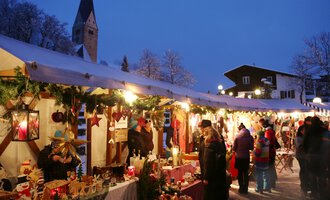 © Kleinwalsertal Tourismus | Frank Drechsel A festive Christmas market with numerous stalls under a tent. It is dark, and the lighting creates an inviting atmosphere. | © Kleinwalsertal Tourismus | Frank Drechsel
