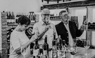 Eine Gruppe von drei Personen genießt Wein in einem Weingeschäft. Sie halten Gläser in der Hand und schauen interessiert in die Gläser. | © Das Naturhotel Chesa Valisa