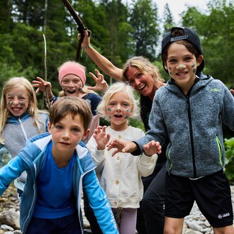 © Kleinwalsertal Tourismus | Oliver Farys Eine Gruppe von Kindern und einem Erwachsenen, die am Ufer eines Flusses stehen. Sie haben Spaß und posieren mit fröhlichen Gesichtsausdrücken. | © Kleinwalsertal Tourismus | Oliver Farys