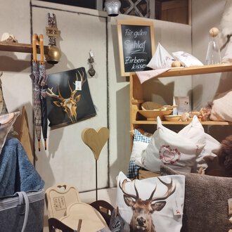 A cozy room with various cushions and decorative items. On a shelf, there are items with animal motifs and wooden accessories. | © Abler Mittelberg | N. Lughammer