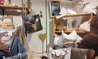 A cozy room with various cushions and decorative items. On a shelf, there are items with animal motifs and wooden accessories. | © Abler Mittelberg | N. Lughammer