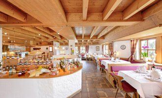 Ein einladendes Restaurant mit Holzdecke und Tischen, die für Gäste gedeckt sind. Im Hintergrund ist eine Auswahl an Marmeladen und Speisen auf einem Buffet sichtbar. | © Alpengasthof Hörnlepass | Monschau Michael