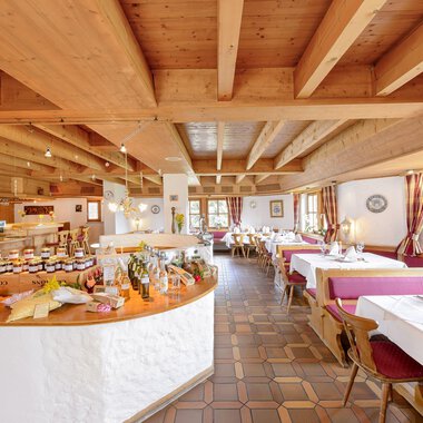 Ein einladendes Restaurant mit Holzdecke und Tischen, die für Gäste gedeckt sind. Im Hintergrund ist eine Auswahl an Marmeladen und Speisen auf einem Buffet sichtbar. | © Alpengasthof Hörnlepass | Monschau Michael