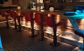 A cozy bar with red high stools and a wooden counter. The room is softly lit, creating a relaxed atmosphere. | © Hotel Steinbock