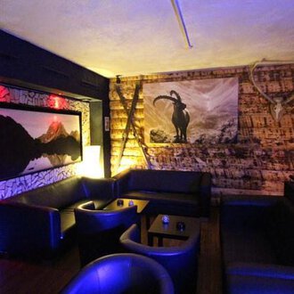 Ein gemütlicher Innenraum mit dunklen Ledermöbeln und einer Holzverkleidung. An der Wand hängt ein Bild eines Bergpanoramas und ein stilisiertes Ziegenmotiv. | © Heiko Möller m&m bar