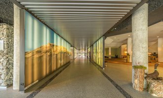 A modern hallway with large wall pictures and an open reception area. The walls are designed with soft colors and beautiful landscapes. | © Kleinwalsertal Tourismus |  Steffen Berschin