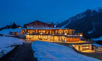 A modern building in the mountains, surrounded by snow and a clear, blue sky. The warm lights of the house create an inviting atmosphere at twilight. | © Hotel Birkenhöhe | Fotos GA Service Salzburg