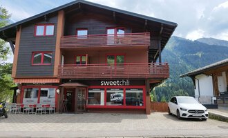 A modern building with a restaurant called "sweetchili" on the ground floor. In the background, green mountains and a blue sky can be seen. | © Kleinwalsertal Tourismus | N. Lughammer