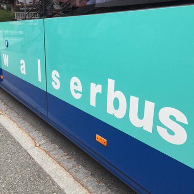 Ein Bus mit der Aufschrift „walserbus“ auf der Seite. Die Farben des Busses sind in Aqua- und Blautönen gehalten. | © Kleinwalsertal Tourismus