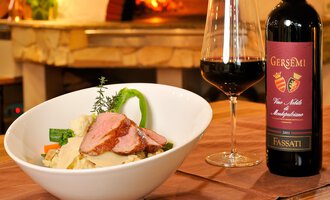 Ein köstlicher Teller mit Fleisch und Gemüse, serviert in einer weißen Schüssel. Neben dem Gericht stehen ein Glas Rotwein und eine Flasche Wein auf dem Tisch. | © Ristorante Trentino | Michael Monschau