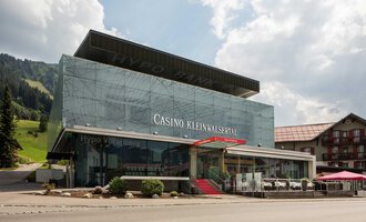 A modern casino with a glass façade in a mountainous setting. There are terraces and seating areas in front of the building. | © Casinos Austria | Arnd Ötting