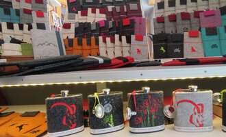 A selection of stylish bottles in various designs is displayed on a shelf. In the background, many colorful accessories and bags can be seen. | © Chrömle Schönes aus Filz | N. Lughammer