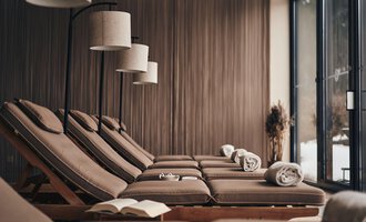 A relaxing wellness area with comfortable loungers and soft lighting. Large windows offer a view of nature. | © Travel Charme Ifen Hotel